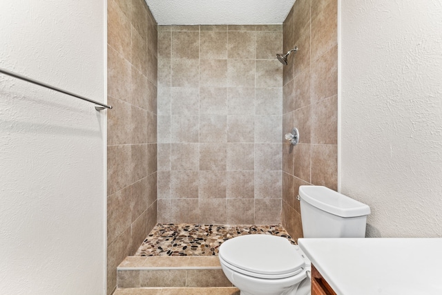 bathroom featuring vanity, tiled shower, a textured ceiling, and toilet