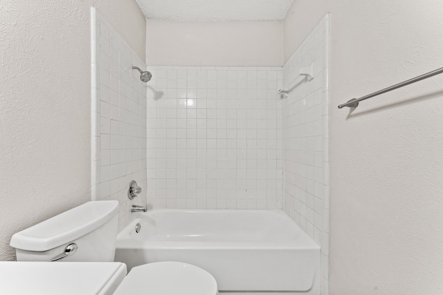 bathroom featuring tiled shower / bath, toilet, and a textured ceiling