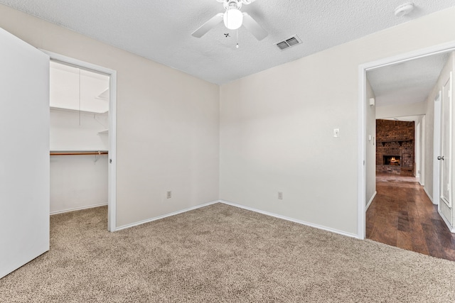 unfurnished bedroom featuring a spacious closet, a textured ceiling, carpet floors, a closet, and ceiling fan