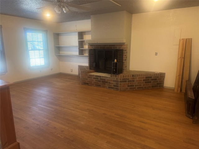 unfurnished living room featuring hardwood / wood-style flooring, ceiling fan, a brick fireplace, and a textured ceiling