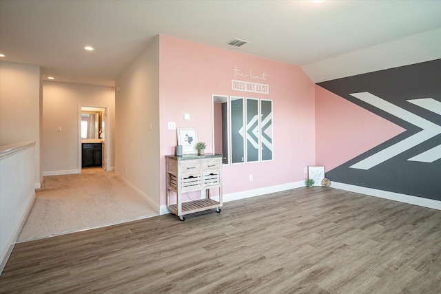 interior space featuring baseboards, visible vents, vaulted ceiling, and wood finished floors