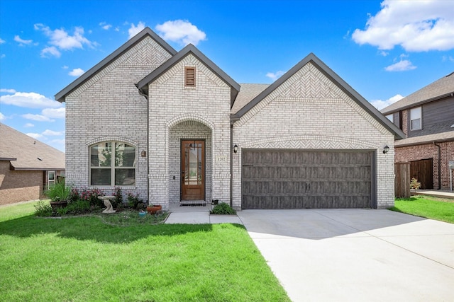 french provincial home with an attached garage, driveway, a front yard, and brick siding