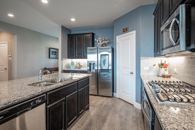 kitchen featuring decorative backsplash, appliances with stainless steel finishes, light stone countertops, light wood-type flooring, and a sink