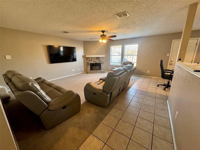 tiled living room with ceiling fan, a stone fireplace, and a textured ceiling