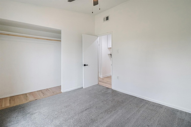 unfurnished bedroom with ceiling fan, carpet flooring, a closet, and a high ceiling