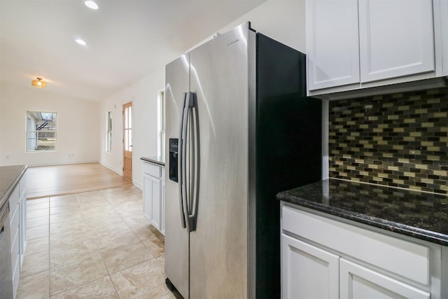 kitchen featuring lofted ceiling, dark stone countertops, stainless steel fridge, decorative backsplash, and white cabinets