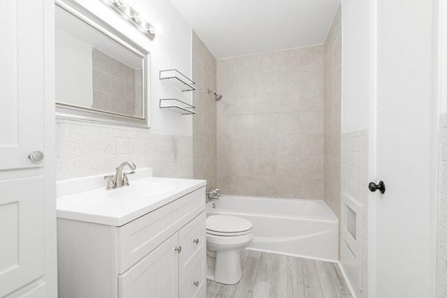 full bathroom featuring tiled shower / bath, tile walls, hardwood / wood-style flooring, vanity, and toilet