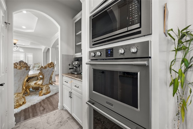 kitchen featuring built in microwave, white cabinetry, light stone countertops, and stainless steel oven