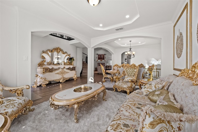 living room with a raised ceiling, ornamental molding, hardwood / wood-style floors, and an inviting chandelier