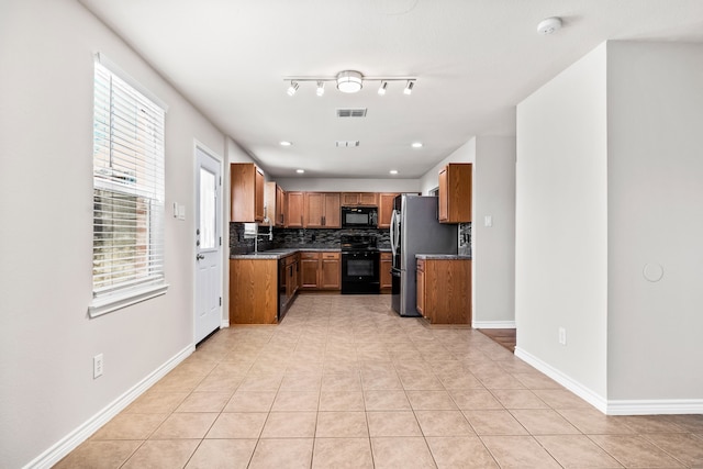 kitchen featuring black microwave, a sink, backsplash, range, and brown cabinetry