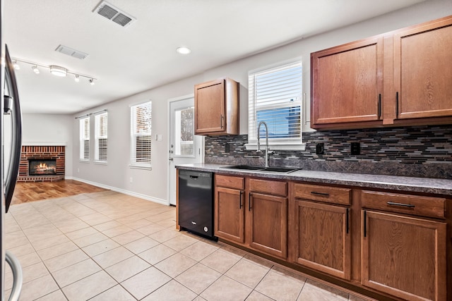 kitchen with light tile patterned floors, a sink, visible vents, black dishwasher, and a brick fireplace