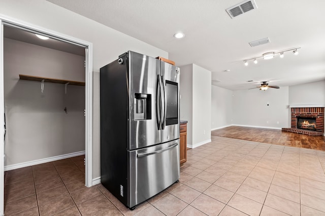 kitchen with light tile patterned flooring, a fireplace, a ceiling fan, visible vents, and stainless steel fridge with ice dispenser