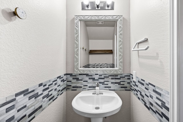 bathroom featuring a textured wall, a sink, and tile walls