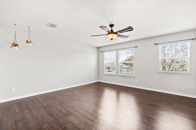 empty room featuring dark wood-style floors, visible vents, and baseboards