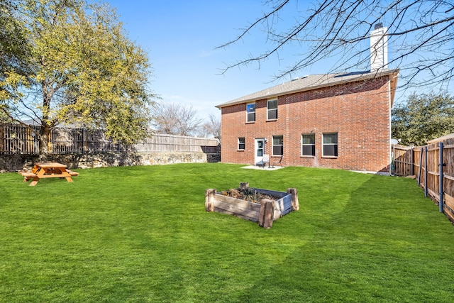 rear view of property with brick siding, a lawn, a chimney, and a fenced backyard