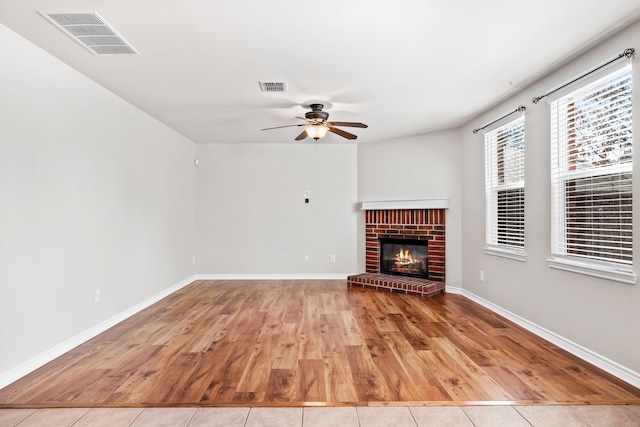 unfurnished living room with a brick fireplace, visible vents, baseboards, and wood finished floors