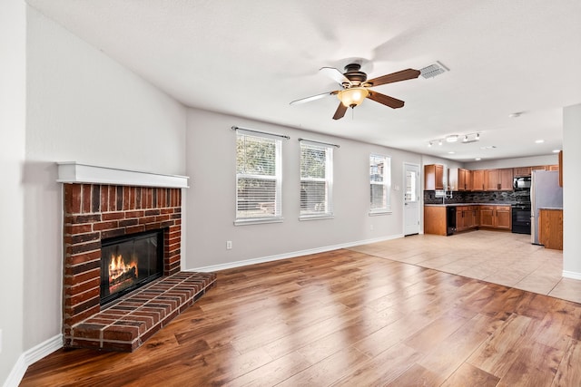 unfurnished living room featuring a brick fireplace, visible vents, light wood-style flooring, and baseboards