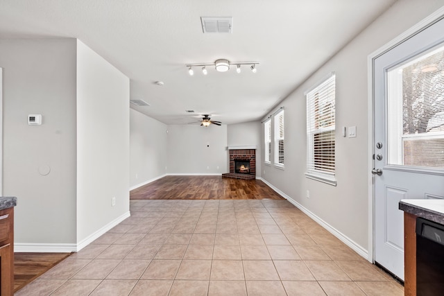 living room with visible vents, a ceiling fan, a brick fireplace, light tile patterned flooring, and baseboards