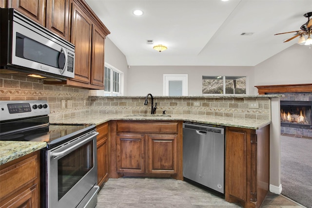 kitchen featuring light stone counters, appliances with stainless steel finishes, a fireplace, and sink