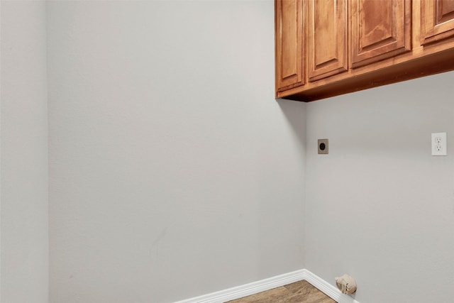 laundry area featuring electric dryer hookup, cabinet space, baseboards, and wood finished floors