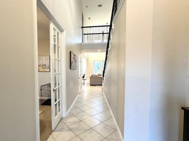 hallway with a towering ceiling, french doors, and light tile patterned flooring