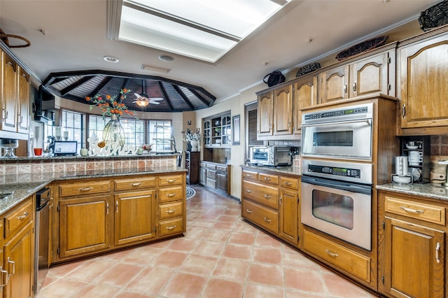 kitchen featuring stone countertops, double oven, lofted ceiling, decorative backsplash, and ceiling fan