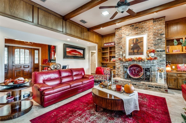 tiled living room featuring built in shelves, beam ceiling, wood walls, ceiling fan, and a fireplace