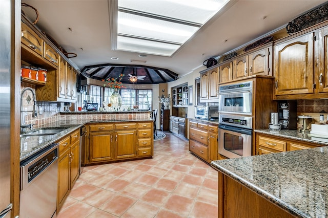 kitchen with sink, appliances with stainless steel finishes, kitchen peninsula, stone counters, and backsplash