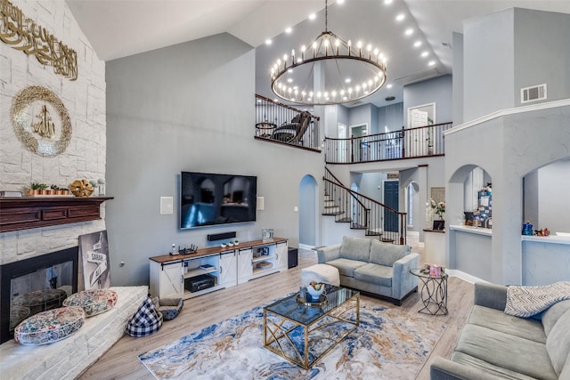 living room featuring an inviting chandelier, hardwood / wood-style floors, a stone fireplace, and high vaulted ceiling