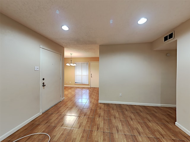 spare room with an inviting chandelier, wood-type flooring, and a textured ceiling