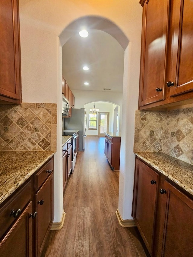 kitchen featuring stainless steel appliances, light stone counters, tasteful backsplash, dark hardwood / wood-style flooring, and a chandelier