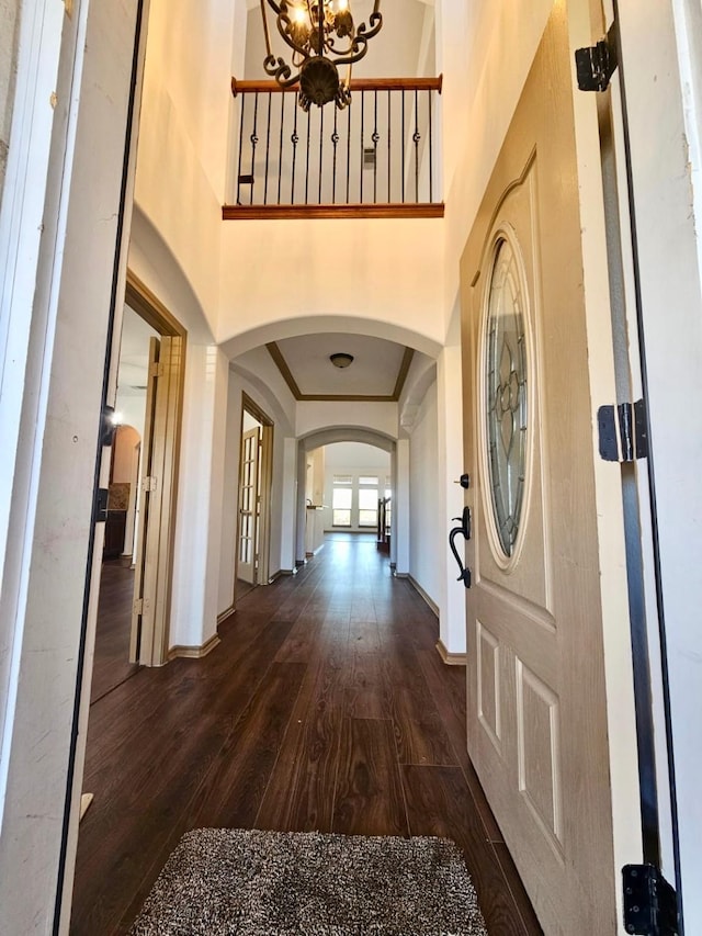 interior space with dark wood-type flooring, ornamental molding, an inviting chandelier, and a high ceiling