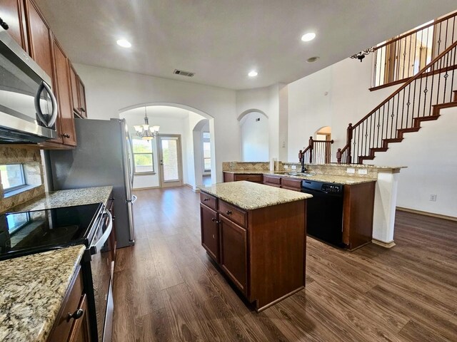 kitchen featuring light stone counters, dark hardwood / wood-style flooring, stainless steel fridge, kitchen peninsula, and a towering ceiling