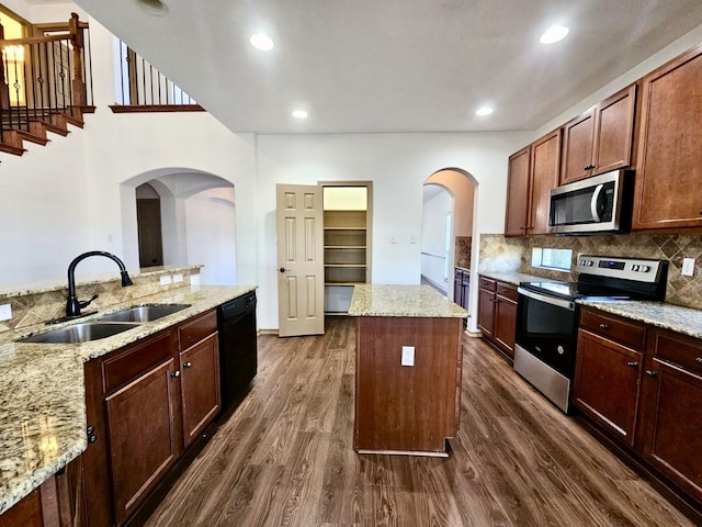 kitchen featuring sink, appliances with stainless steel finishes, a center island, light stone countertops, and dark hardwood / wood-style flooring