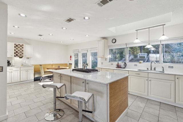 kitchen with sink, a kitchen breakfast bar, a center island, light stone countertops, and decorative backsplash