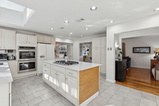 kitchen featuring white cabinetry, light stone counters, a center island, light tile patterned floors, and stainless steel appliances