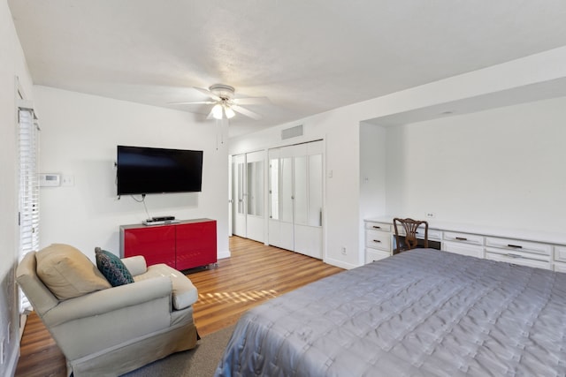 bedroom with built in desk, light hardwood / wood-style floors, a closet, and ceiling fan