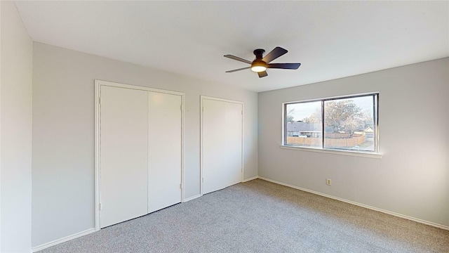 unfurnished bedroom featuring multiple closets, carpet flooring, and ceiling fan