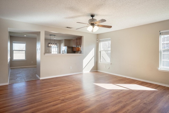 unfurnished living room with wood-type flooring, a wealth of natural light, a textured ceiling, and ceiling fan