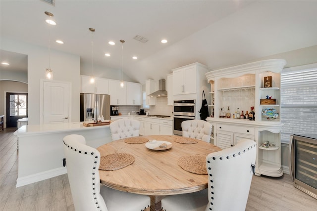 dining space with vaulted ceiling, beverage cooler, and light hardwood / wood-style floors