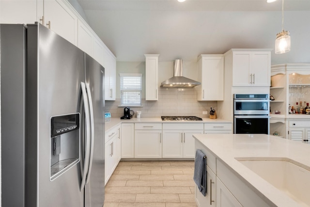 kitchen with hanging light fixtures, white cabinetry, appliances with stainless steel finishes, and wall chimney range hood