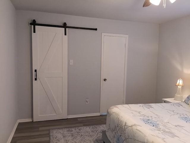 bedroom with a barn door, dark wood-type flooring, and ceiling fan