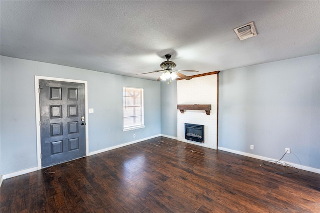 unfurnished living room with dark wood-type flooring, ceiling fan, a fireplace, and a textured ceiling