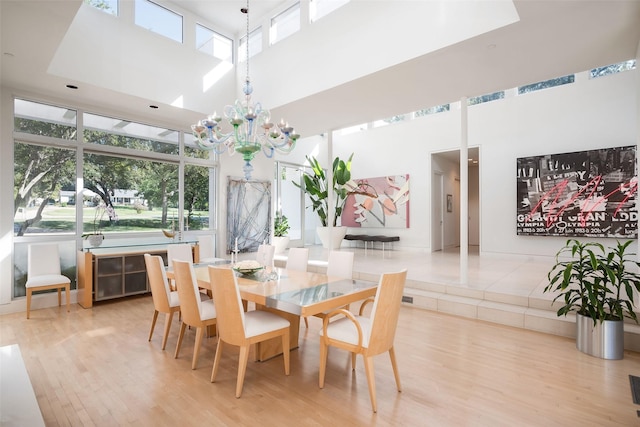 dining room with a towering ceiling, a notable chandelier, and light hardwood / wood-style flooring