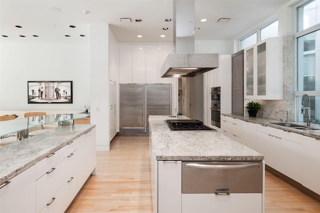 kitchen featuring sink, white cabinetry, light stone counters, island range hood, and stainless steel appliances