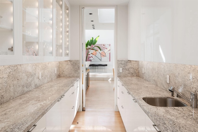 kitchen with sink, white cabinets, backsplash, light stone countertops, and light wood-type flooring