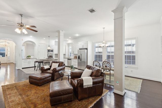 living room with ornamental molding, ceiling fan with notable chandelier, dark wood-type flooring, and decorative columns