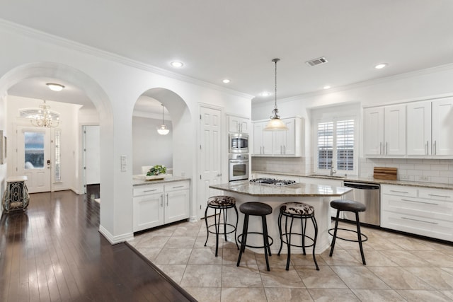 kitchen with appliances with stainless steel finishes, white cabinetry, hanging light fixtures, a center island, and light stone counters