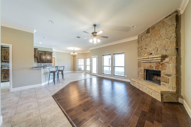 unfurnished living room with ornamental molding, a fireplace, ceiling fan with notable chandelier, and light tile patterned floors