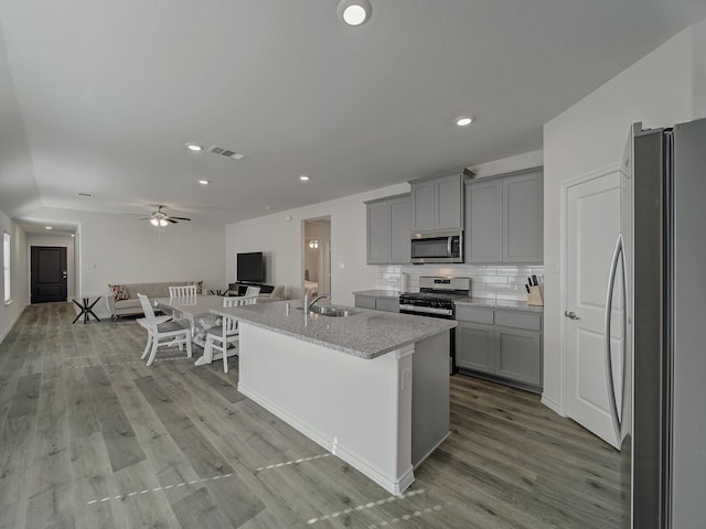 kitchen featuring sink, gray cabinetry, a center island with sink, stainless steel appliances, and decorative backsplash